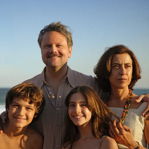 Family of four at the beach posing together, smiling, with ocean in the background at sunset.