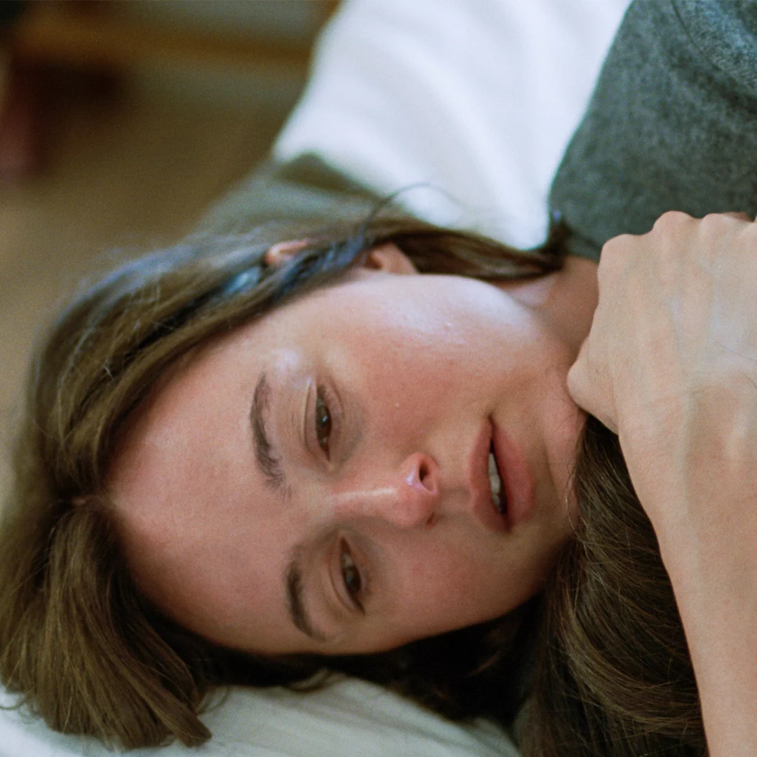 Woman lying on her side with her head on a pillow, eyes half-closed, looking tired or sleepy.
